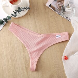 Pink thong on a wooden surface with a cup, plant, and magazine in the background.