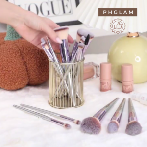 Makeup brushes in a holder with lip products on a table, featuring the PHGLAM brand.